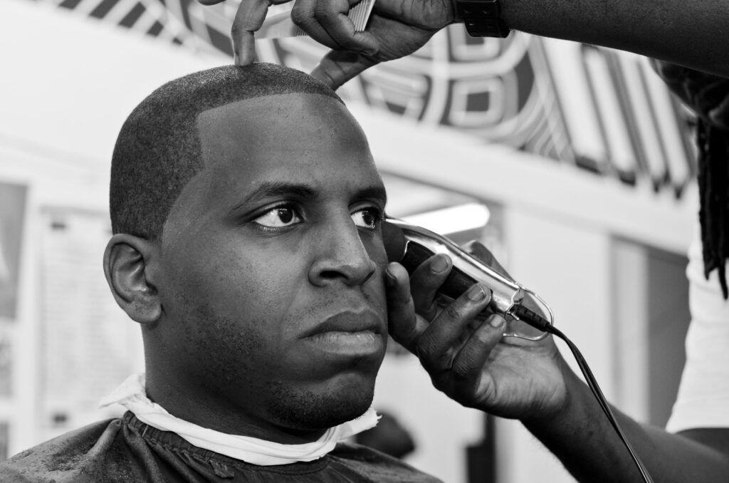 Black and White photograph of the groom getting his hair done in a barber shop before the wedding.