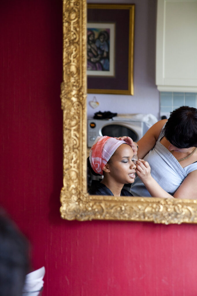 Colour photograph of a reflection in a golden mirror of the bride getting her makeup done before the wedding
